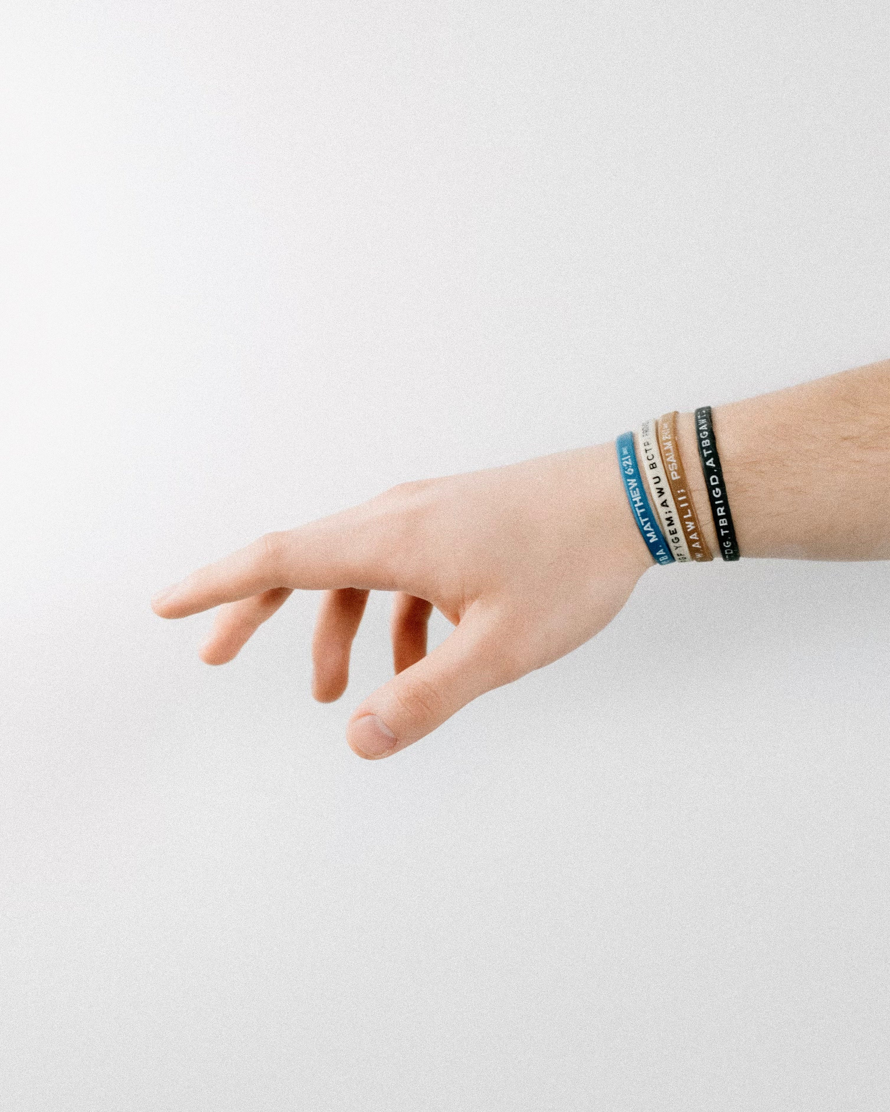 A hand with four Bible memory project wristbands on reaching to the left